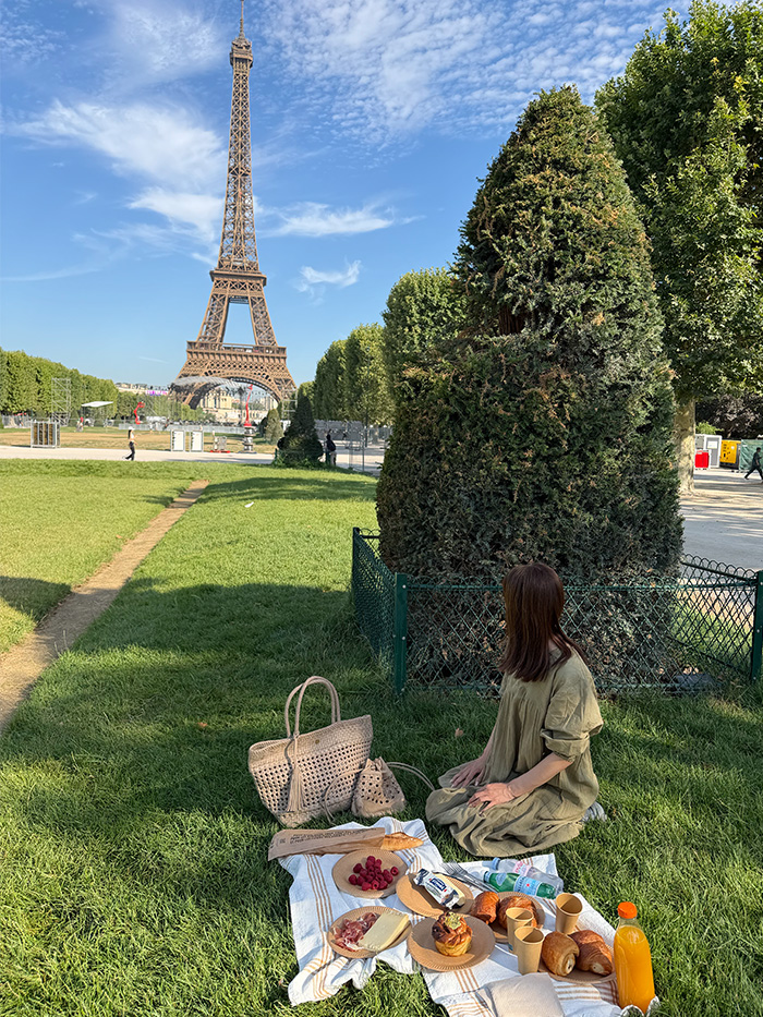 エッフェル塔前の芝生で旅行バッグとピクニックを楽しむ50代女性