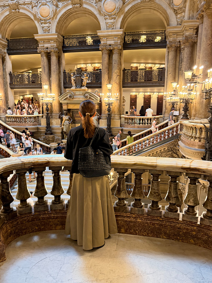 オペラ・ガルニエを本革バッグで訪れる旅行中の50代女性