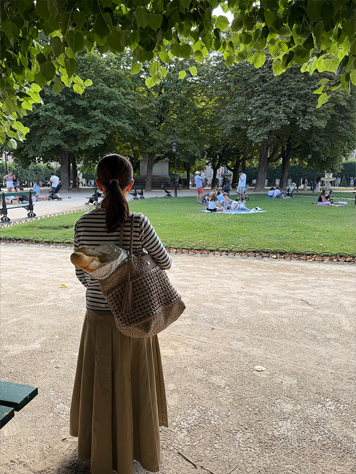 フランス建国記念日のヴォージュ広場で過ごす50代女性と旅行バッグ